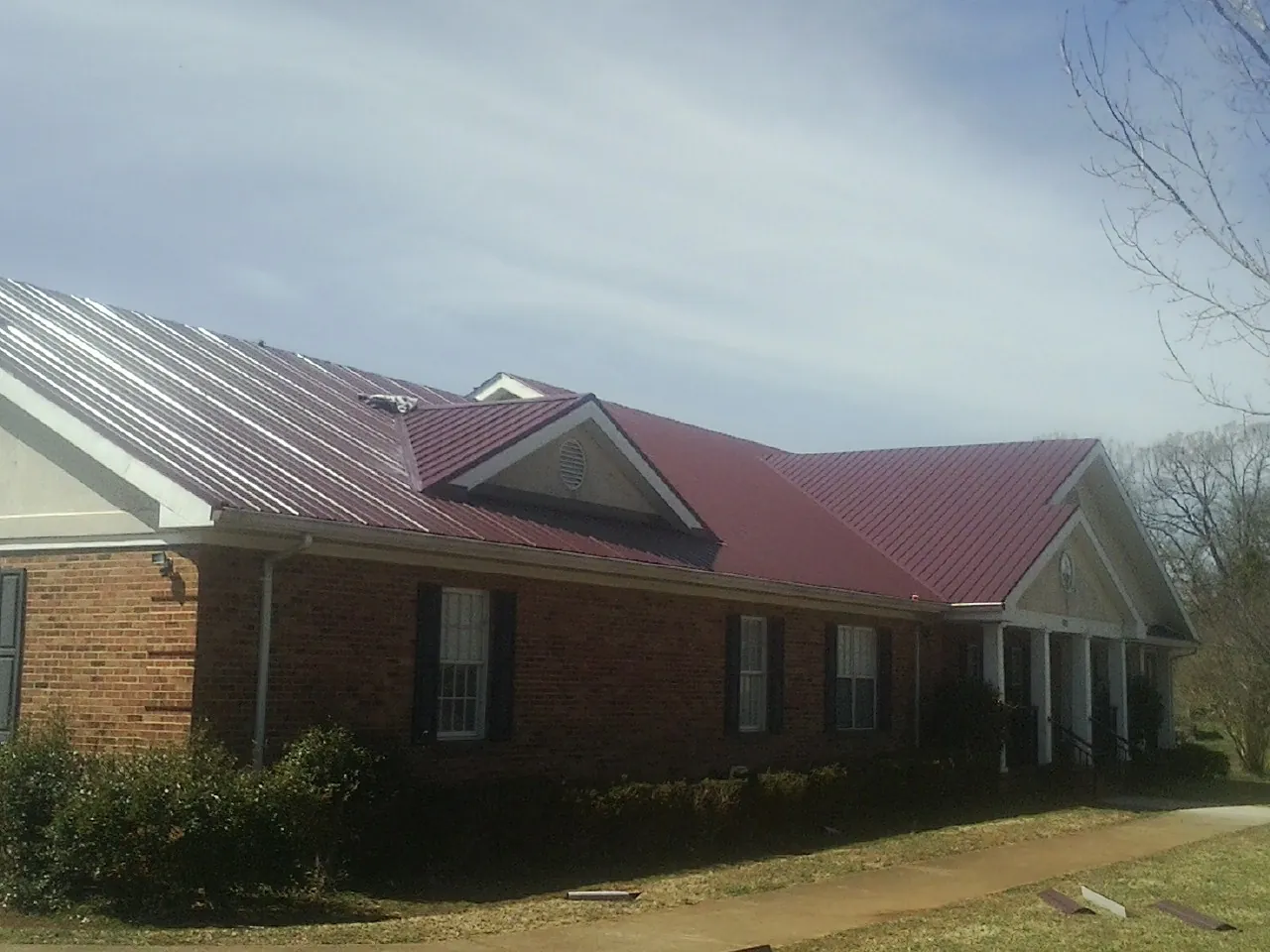 Red metal roof with gabled entries on a long brick building, from a Hail Damage Roof Repair job in Montana Mines
