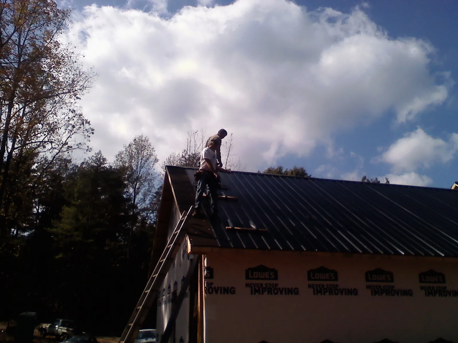 Roofer fastening dark metal panels high against a cloudy sky, from a Roof Inspection job in Montana Mines