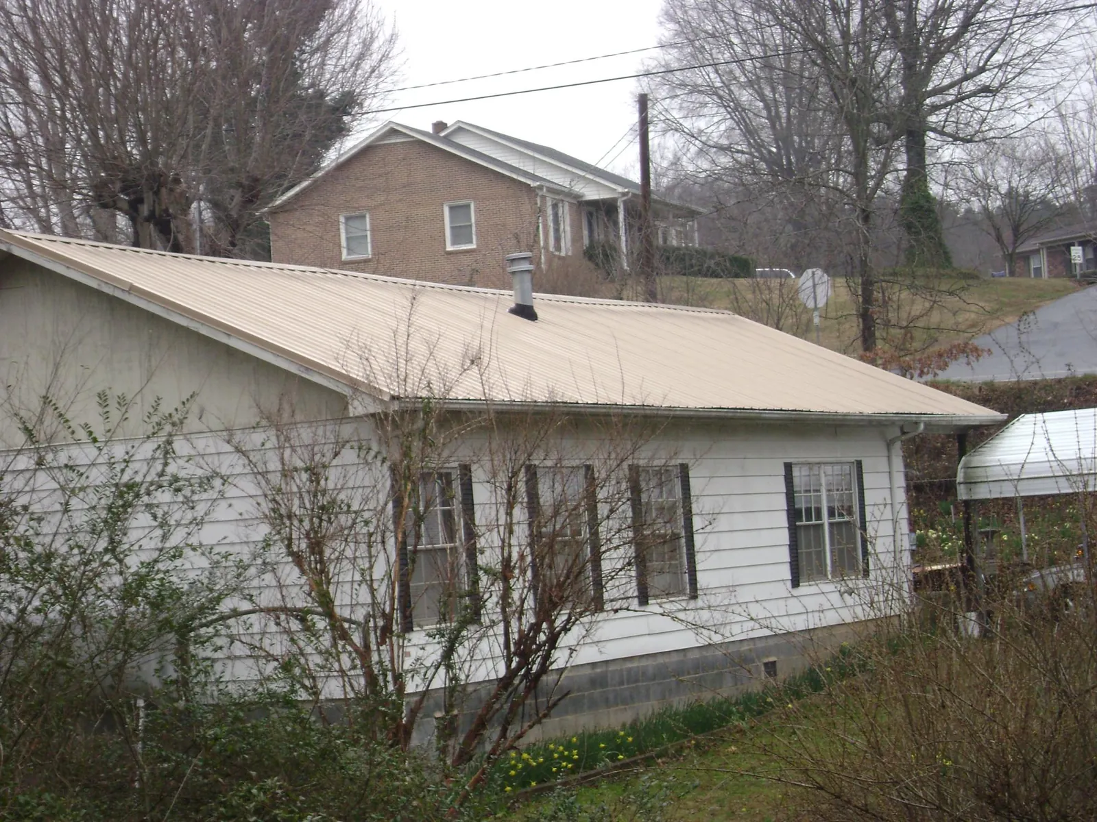 Tan metal roof on a white sided house set into a hillside — Commercial Roofing by Roofing Brothers in Montana Mines